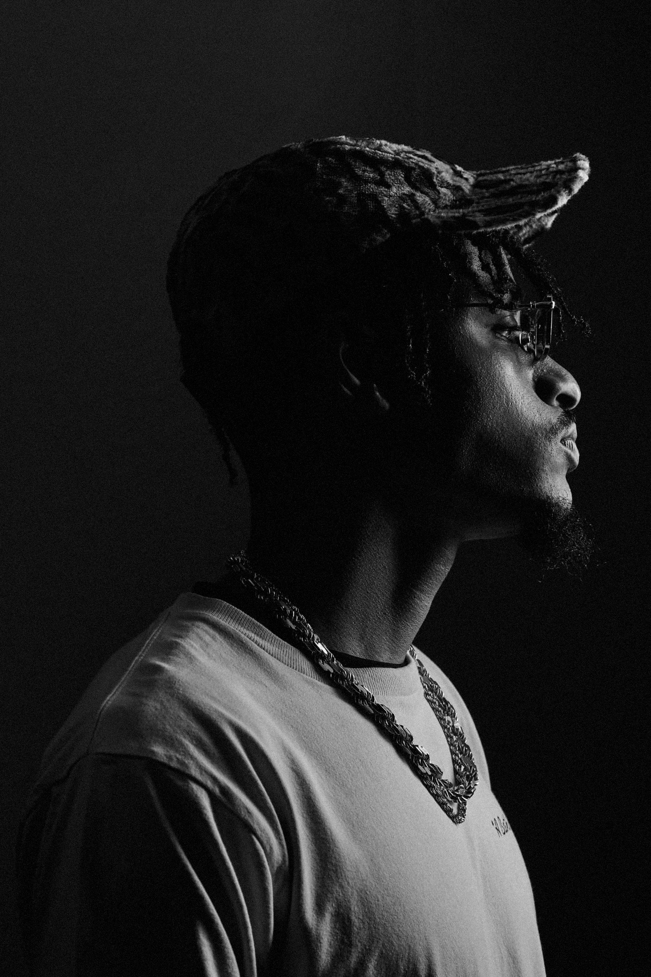 Touché Noir in profile under low light, textured cap and layered chains