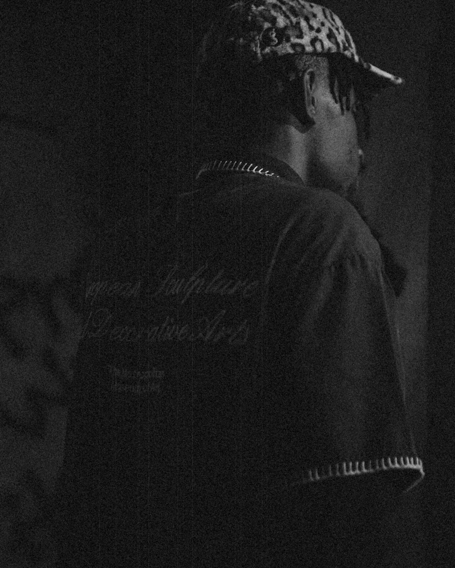 Touché Noir photographed from behind in low light, leopard-print cap and script-printed shirt