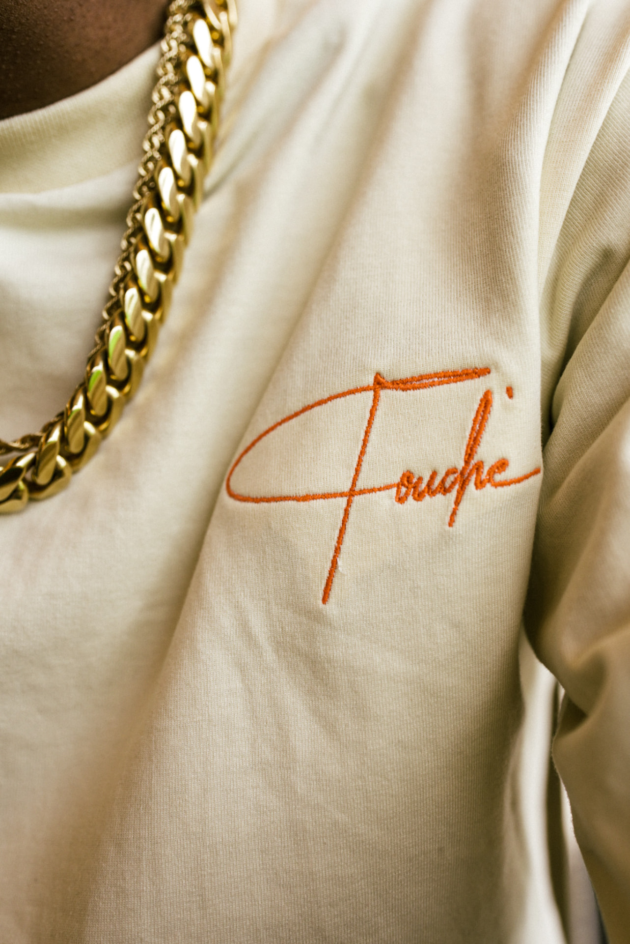 Cream tee with rust-colored Touché script embroidery at the chest